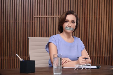 Mature woman with taped mouth in office. Speech censorship