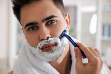 Handsome young man shaving with razor in bathroom