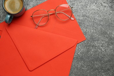 Red envelopes, cup of coffee and glasses on grey table, flat lay. Space for text