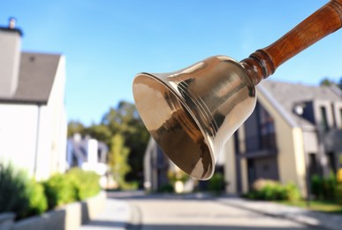 Golden school bell with wooden handle and blurred view of street on sunny day