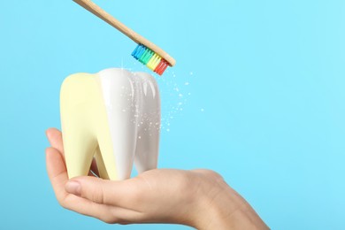 Woman holding ceramic model of tooth and wooden brush on light blue background. Whitening concept