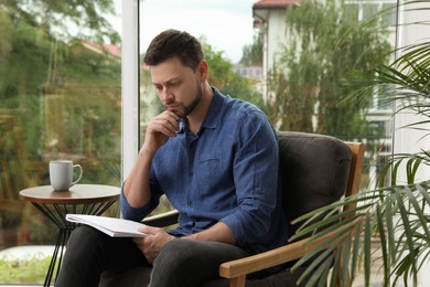 Man solving sudoku puzzle in armchair at home