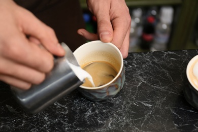 Barista adding milk to coffee at table, closeup