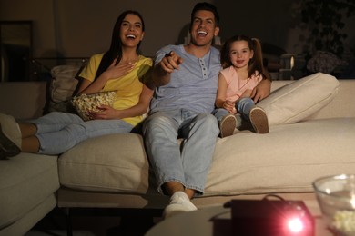 Family watching movie with popcorn on sofa at night
