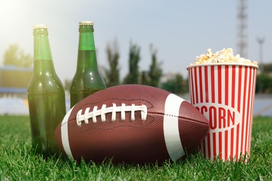 American football ball with beer and popcorn on green field grass in stadium