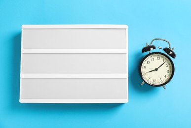 Photo of Blank letter board and alarm clock on light blue background, flat lay