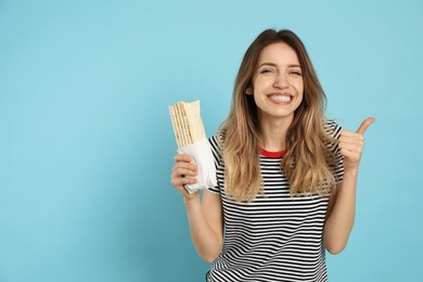 Young woman with delicious shawarma on turquoise background. Space for text