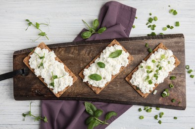 Photo of Crispy crackers with cottage cheese and different herbs on white wooden table, flat lay