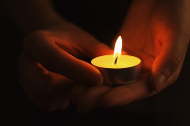 Woman with burning candle in darkness, closeup. Memory day