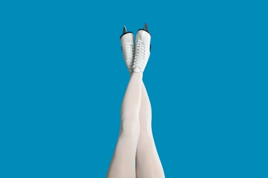 Woman in elegant white ice skates on light blue background, closeup of legs