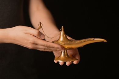 Woman rubbing magical Aladdin lamp on black background, closeup