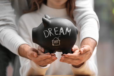Couple holding piggy bank with word DREAM, closeup