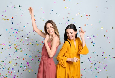 Happy women and falling confetti on light grey background