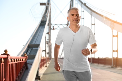 Handsome mature man running on bridge, space for text. Healthy lifestyle
