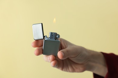 Man holding lighter with burning flame against beige background, closeup