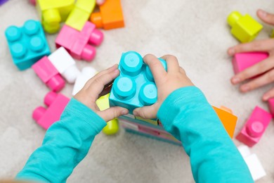 Top view of little child playing with building blocks on carpet, closeup