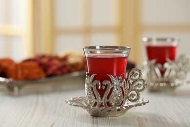 Photo of Glass of traditional Turkish tea in vintage holder on white wooden table