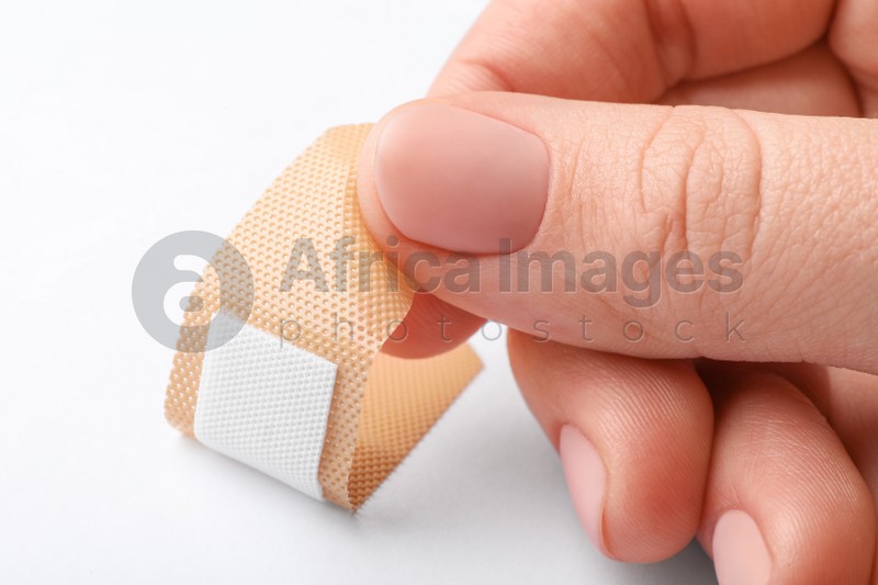 Woman putting sticking plaster on white background, closeup. First aid item