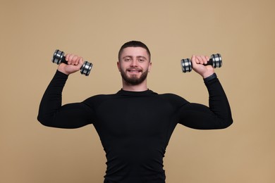 Photo of Handsome sportsman exercising with dumbbells on brown background