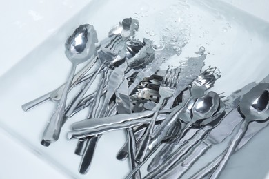Photo of Washing silver spoons, forks and knives in kitchen sink with water, above view