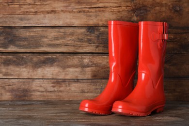 Pair of red rubber boots on wooden surface. Space for text