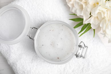 Jar of natural exfoliating salt scrub, white towel and freesia flowers on table, flat lay