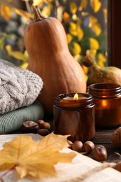 Photo of Burning scented candles, warm sweaters, book and pumpkins on wooden table near window. Autumn coziness