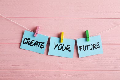 Photo of Paper notes with motivational phrase Create Your Future hanging on pink wooden wall
