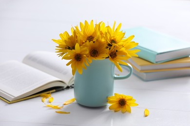 Beautiful bright yellow flowers in light blue cup near books on white table