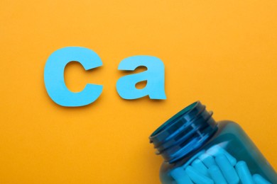 Open bottle and calcium symbol made of light blue letters on orange background, flat lay