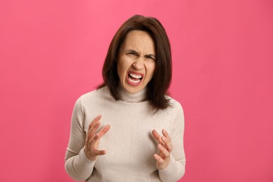 Portrait of screaming woman filled with hate on pink background
