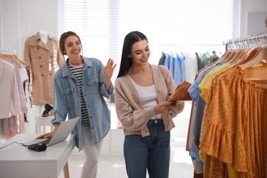 Shop assistant helping customer to choose clothes in modern boutique