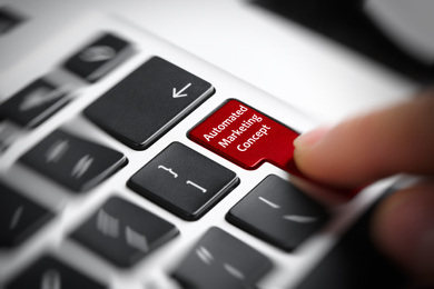 Woman pressing button with text AUTOMATED MARKETING CONCEPT on modern laptop keyboard, closeup