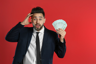 Emotional young man with money on crimson background