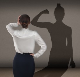 Businesswoman and shadow of strong muscular lady in front of her on grey wall. Concept of inner strength