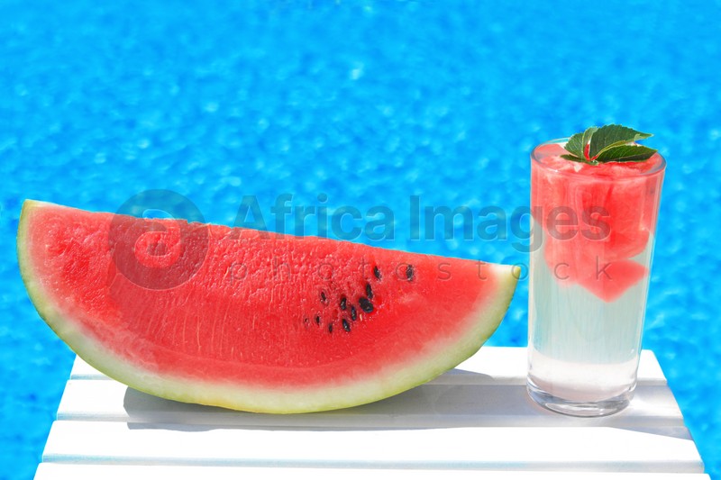 Refreshing drink in glass and sliced watermelon near swimming pool outdoors. Space for text