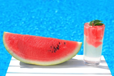 Refreshing drink in glass and sliced watermelon near swimming pool outdoors. Space for text