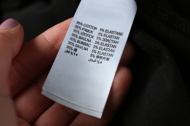 Woman reading clothing label with material content  on black shirt, closeup
