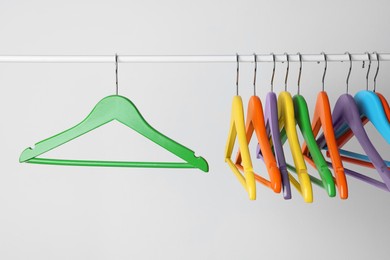 Photo of Bright clothes hangers on metal rail against light background