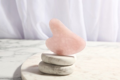 Rose quartz gua sha tool and spa stones on white marble table