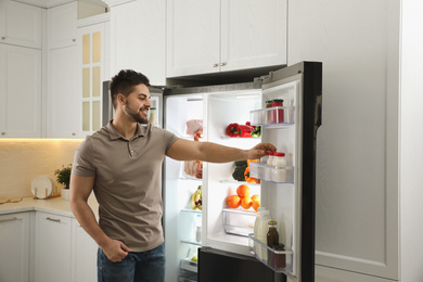 Young man taking yoghurt out of refrigerator in kitchen