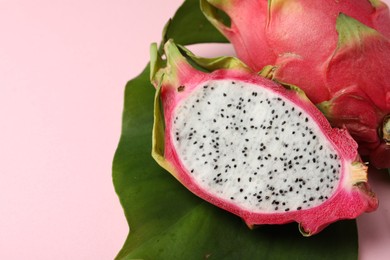 Photo of Delicious cut and whole white pitahaya fruits with green leaf on light pink background