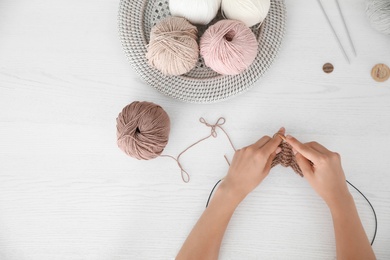 Photo of Top view of young woman knitting with needles at white wooden table, closeup. Engaging in hobby