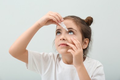 Adorable little girl using eye drops on white background