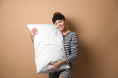 Beautiful woman with pillow on beige background. Bedtime