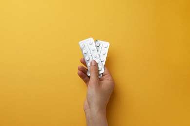 Woman holding blisters of pills on orange background, top view