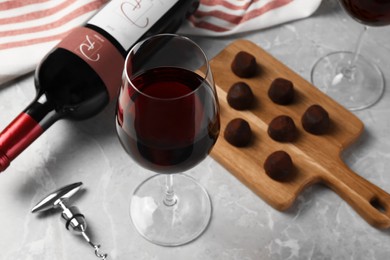 Bottle and glass of red wine with chocolate candies on light marble table