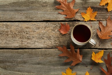 Cup of hot tea and autumn leaves on wooden table, flat lay. Space for text