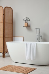 Modern ceramic bathtub and folding screen near white wall in room