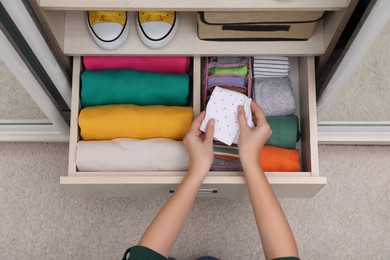 Woman folding clothes in wardrobe drawer indoors, top view. Vertical storage